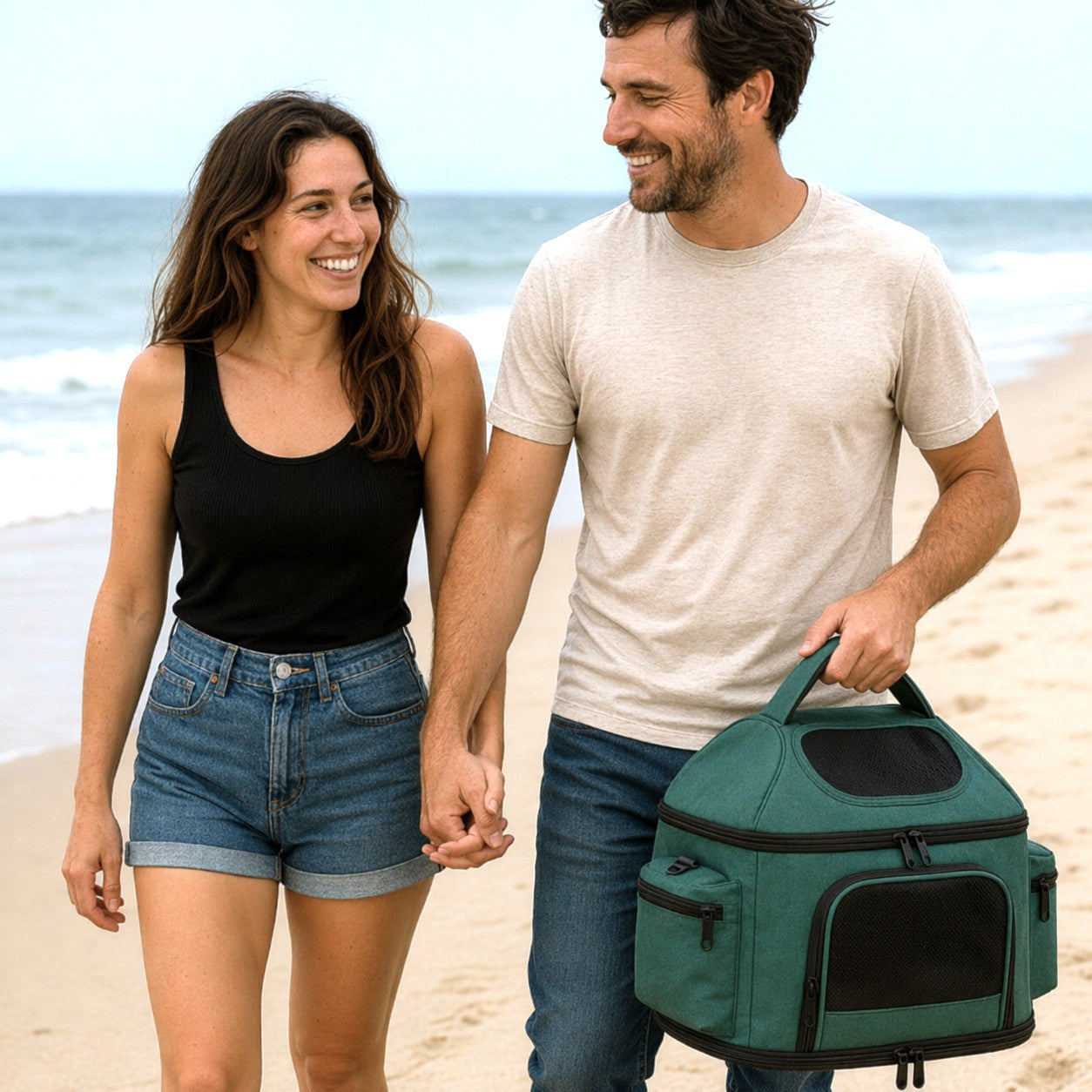 A couple walking hand in hand on the beach with a green Treeho pet carrier